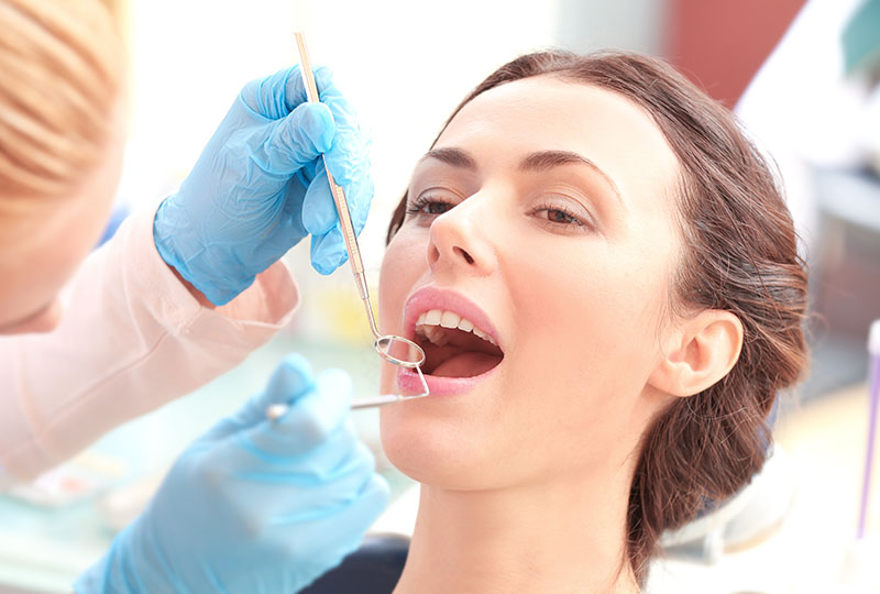 A woman receiving dental treatment with a dentist using a drill on her teeth.