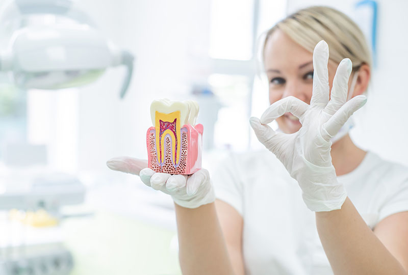 A woman in a white lab coat holds up a small box with a pink inside, while another hand holds up a magnifying glass displaying a pill and a syringe.
